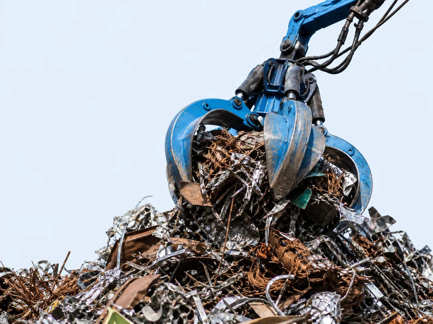 Blue hydraulic grabber lifting mixed scrap metal